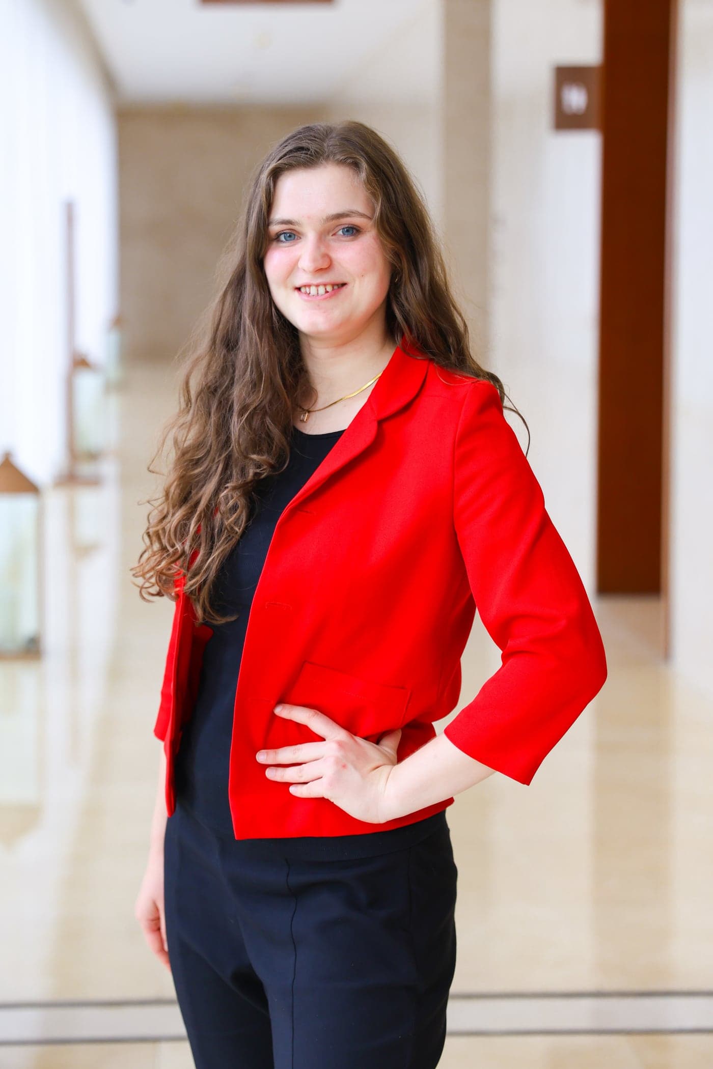Sarah Mayrhofer in a red blazer, standing in a light-filled corridor